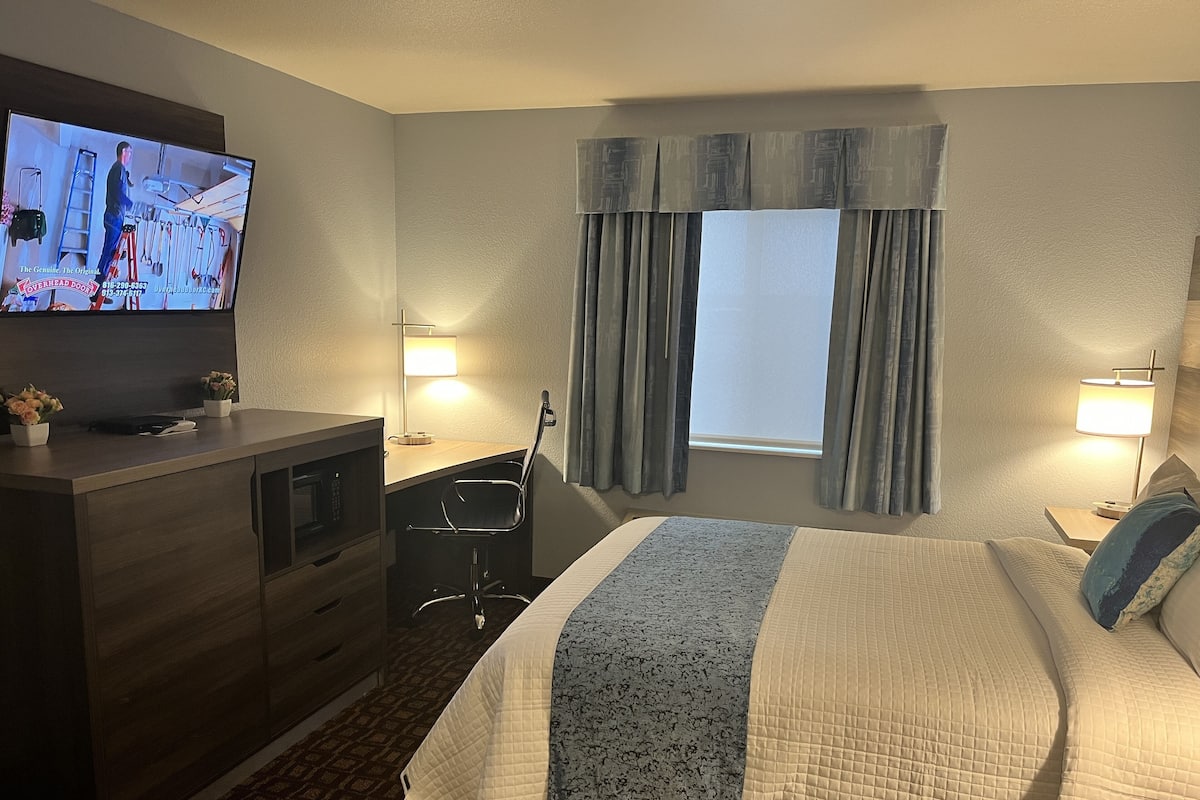 Een hotelkamer met een bed, bureau, stoel, televisie en gordijnen.