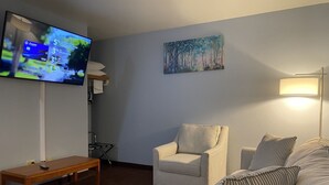 A living room with a television, striped armchairs, a sofa, a wooden table, and a painting on the wall.