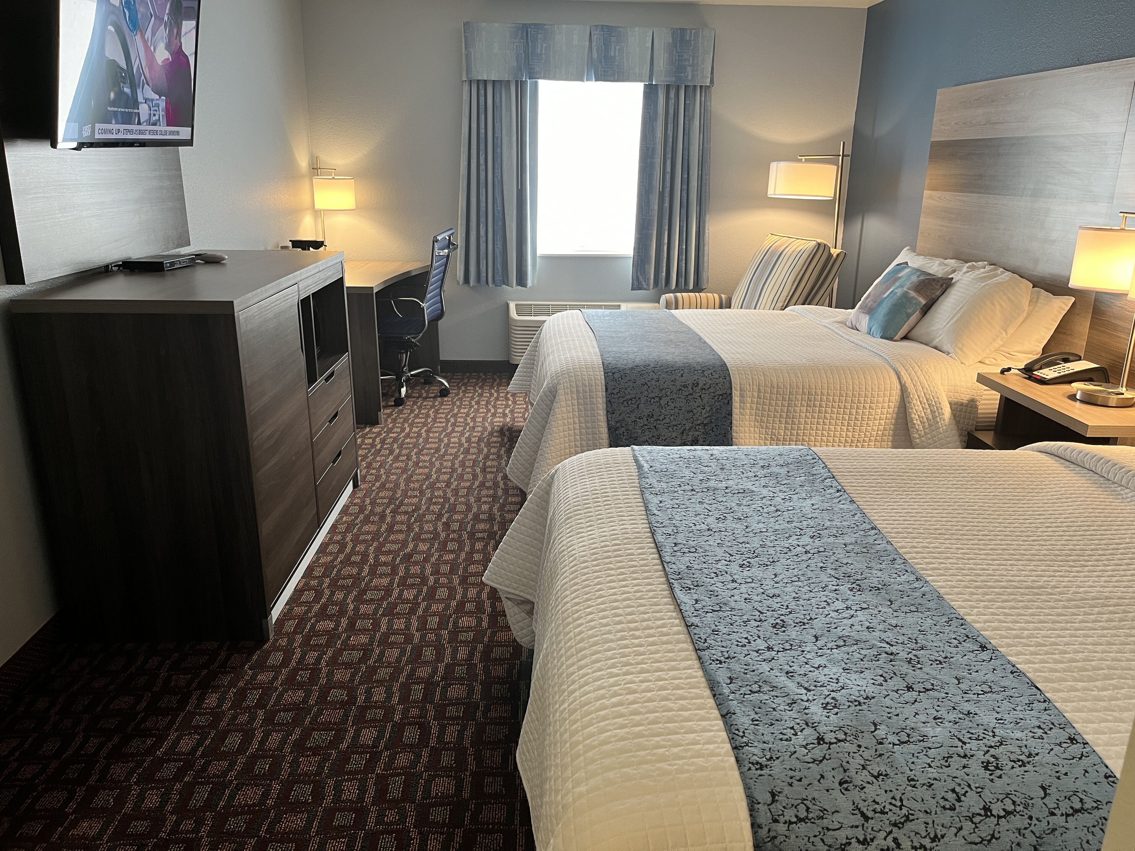 Ein Hotelzimmer mit zwei Betten, einem Schreibtisch, einem Stuhl, einem Schminktisch und einem Fernseher.