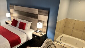 A hotel room with a bed, bedside table with a lamp, a striped armchair, and a bathroom with a bathtub.
