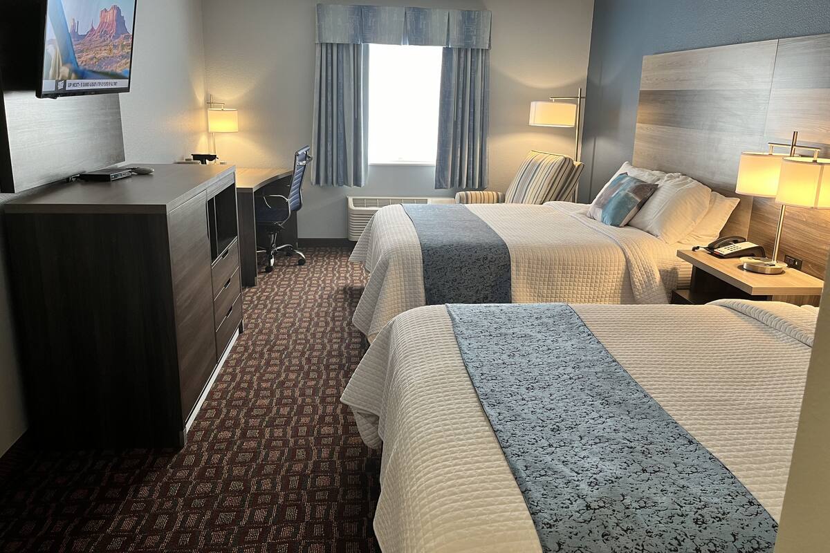 Een hotelkamer met twee bedden, een bureau, een stoel, een televisie en een raam met gordijnen.