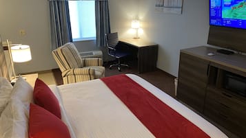 A hotel room with a bed, a desk, a chair, a lamp, a TV, and a window with curtains.