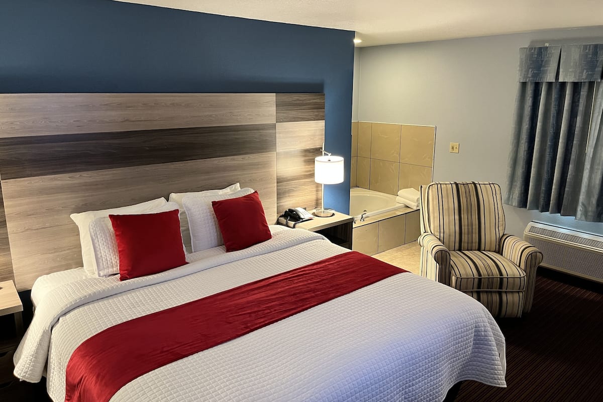 Hotelkamer met een groot bed, nachtkastje, stoel, bureau, lamp, raam met gordijnen, en wand in blauw-grijze kleurstelling.
