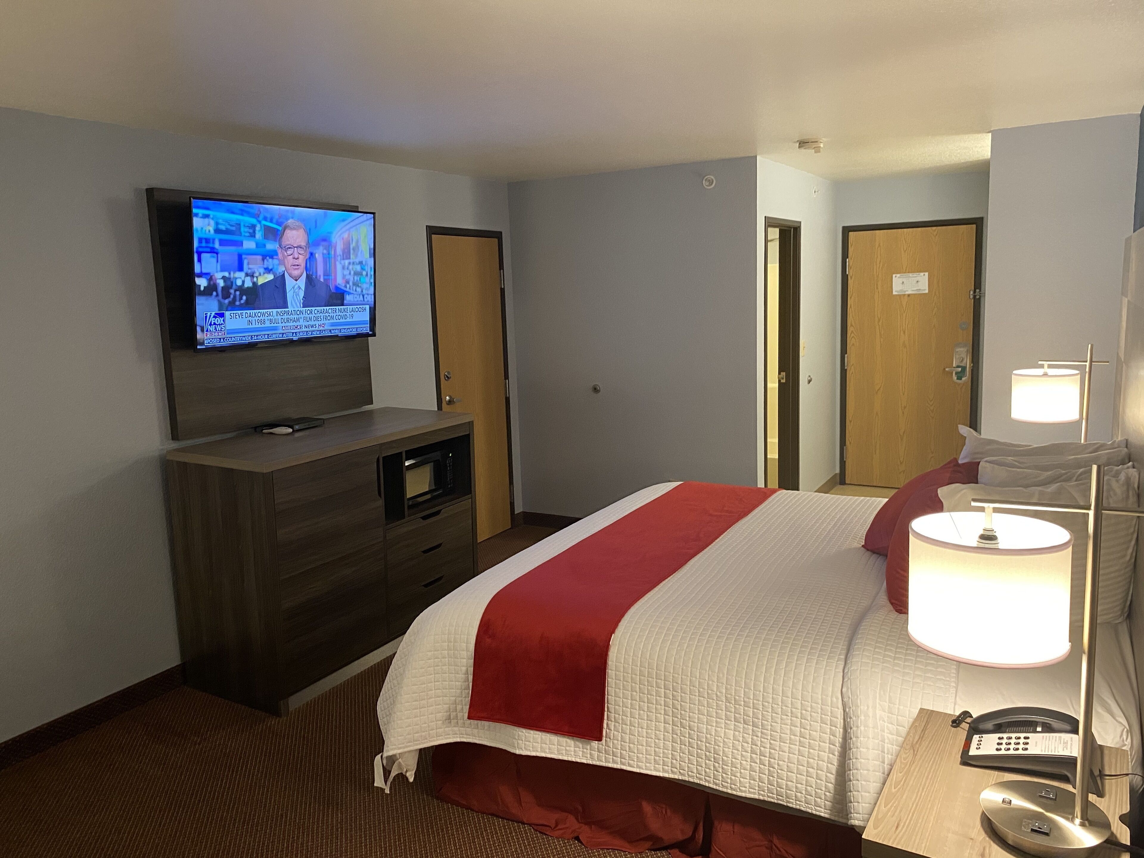 A hotel room with a bed, a TV on a wooden dresser, a bedside lamp, and a phone.