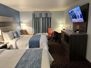 A hotel room with two beds, a desk, a chair, a TV, and a window with curtains. - Garnett Hotel & RV Park (Garnett)