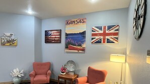 A room with two pink armchairs, a small table with a lamp, and wall decorations including an American flag and a British flag.