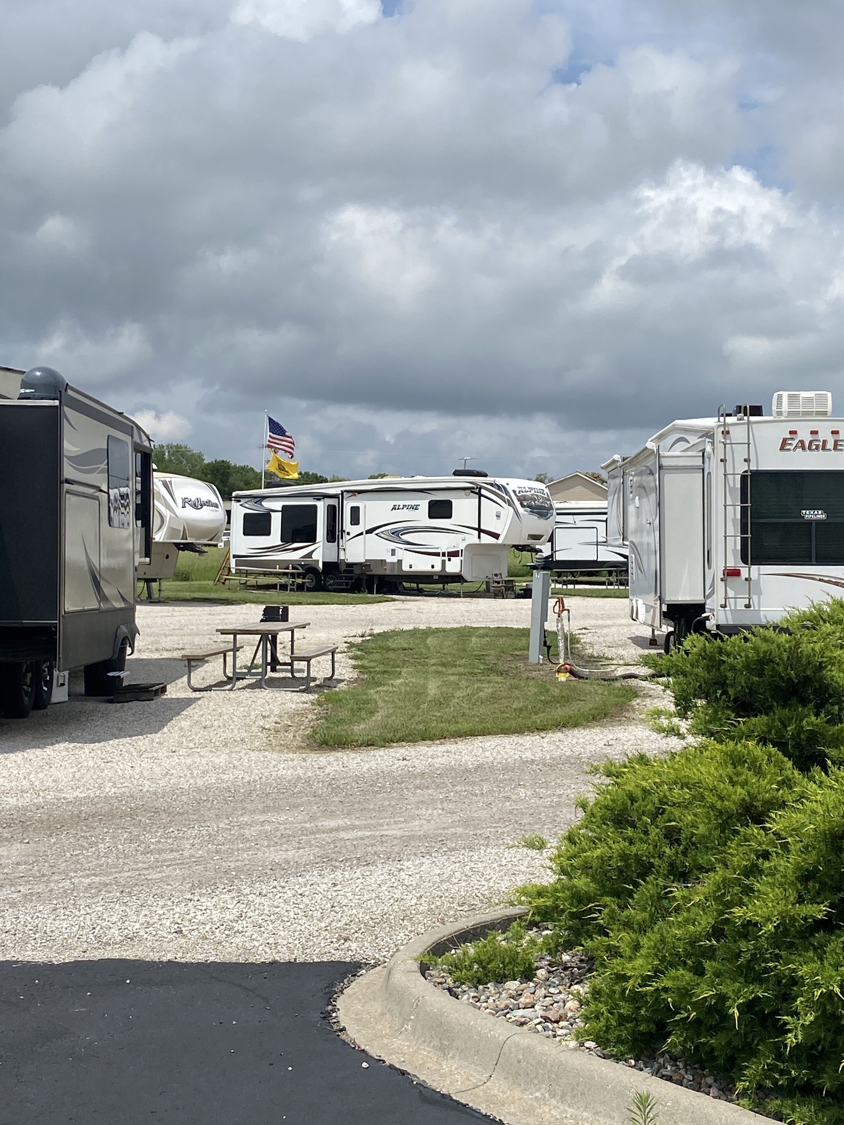 Ein Campingplatz mit Reisemobilen auf Schotter, Picknicktischen und einer Flagge.