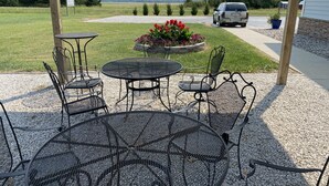 A patio with a round metal table and chairs, surrounded by gravel and a flower bed with red flowers.