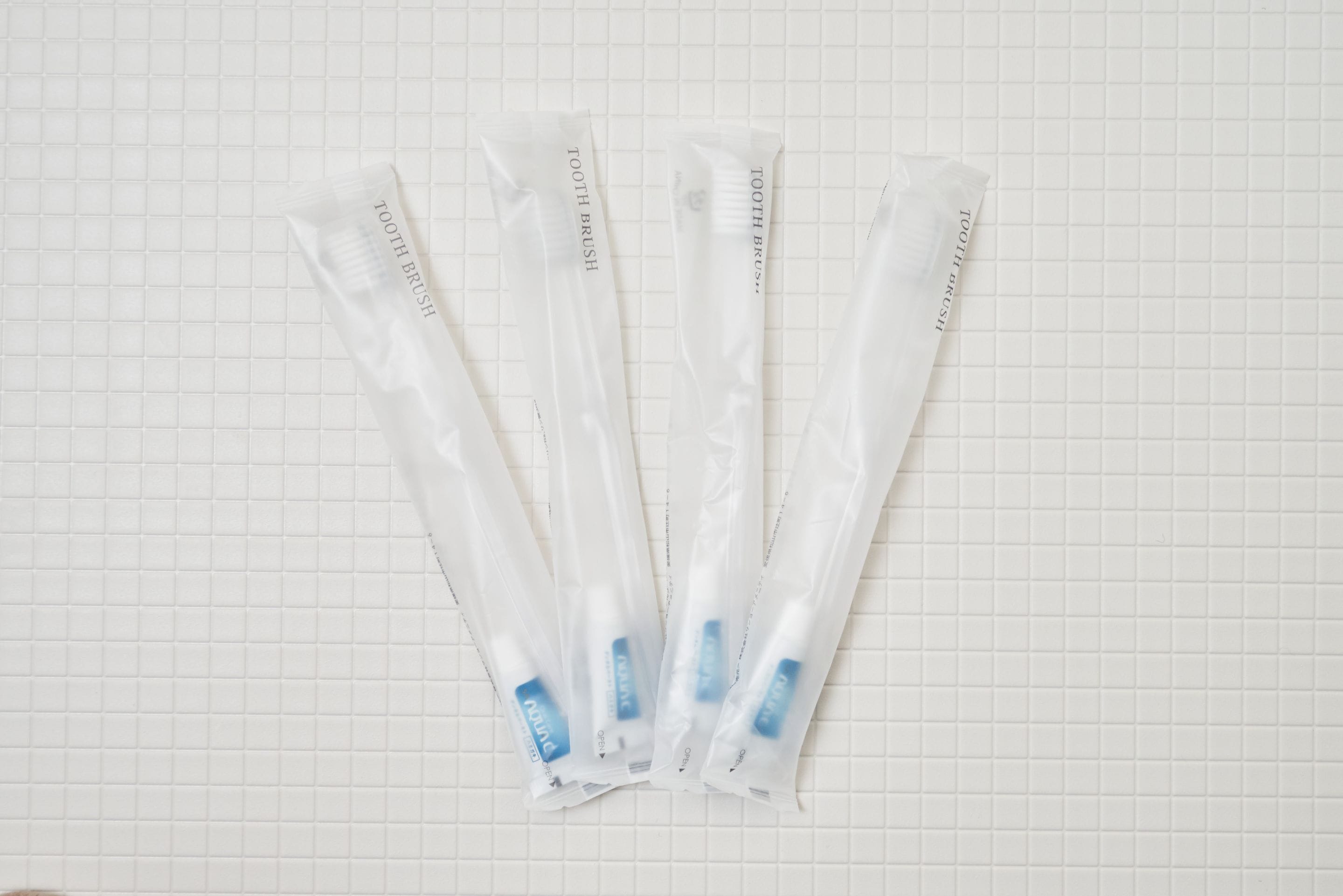 Cinq brosses à dents blanches, dotées d’étiquettes bleues, sont disposées sur une surface carrelée blanche.