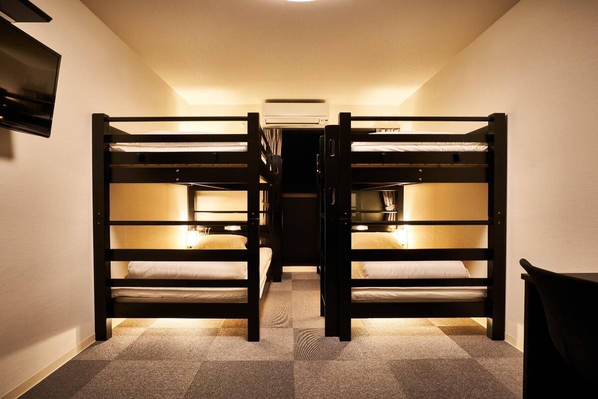 A narrow hallway with two bunk beds, a flat-screen TV mounted on the wall, and a ceiling-mounted air conditioning unit.