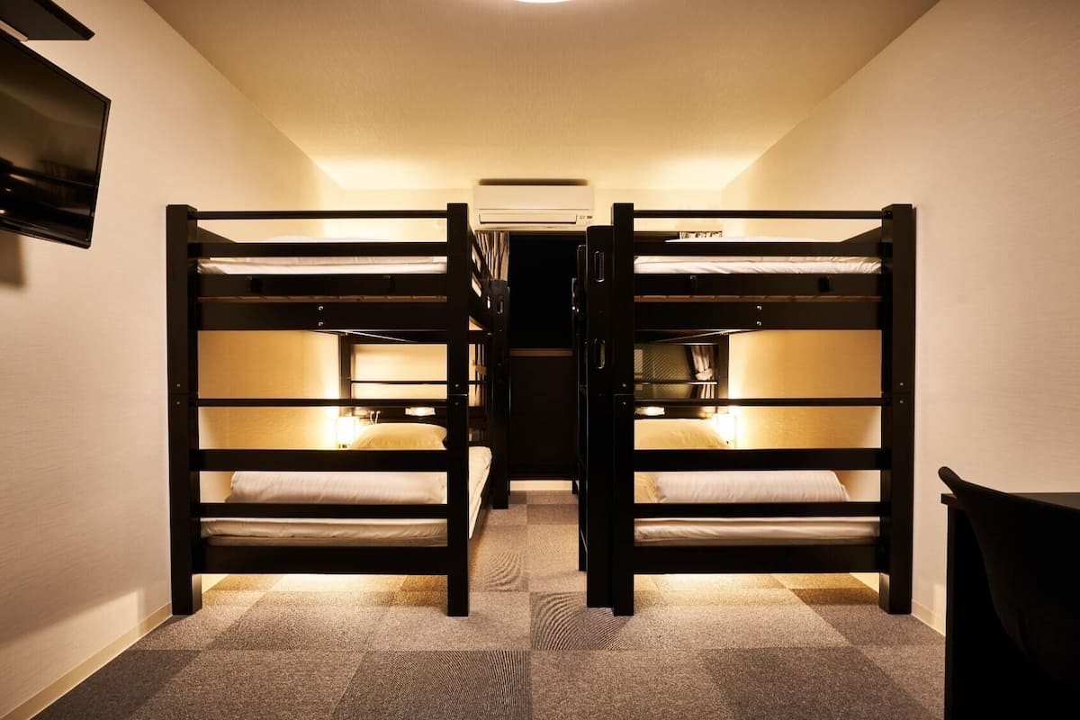A narrow hallway with two bunk beds, a flat-screen TV mounted on the wall, and a ceiling-mounted air conditioning unit.