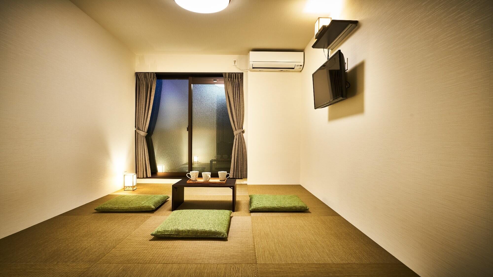 A room with tatami mats, a small table with cups, a TV, and an air conditioning unit.