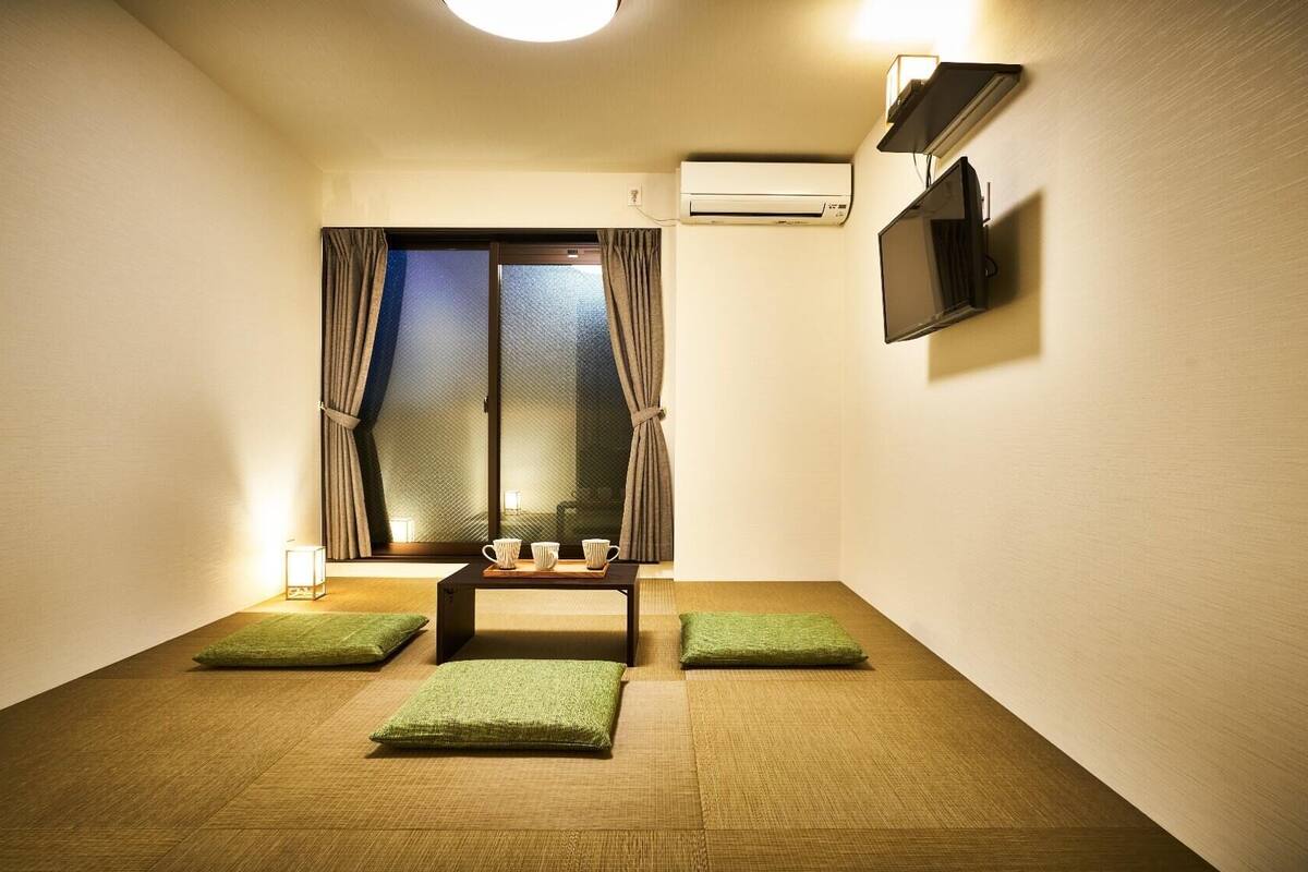 A room with tatami mats, a small table with cups, a TV, and an air conditioning unit.