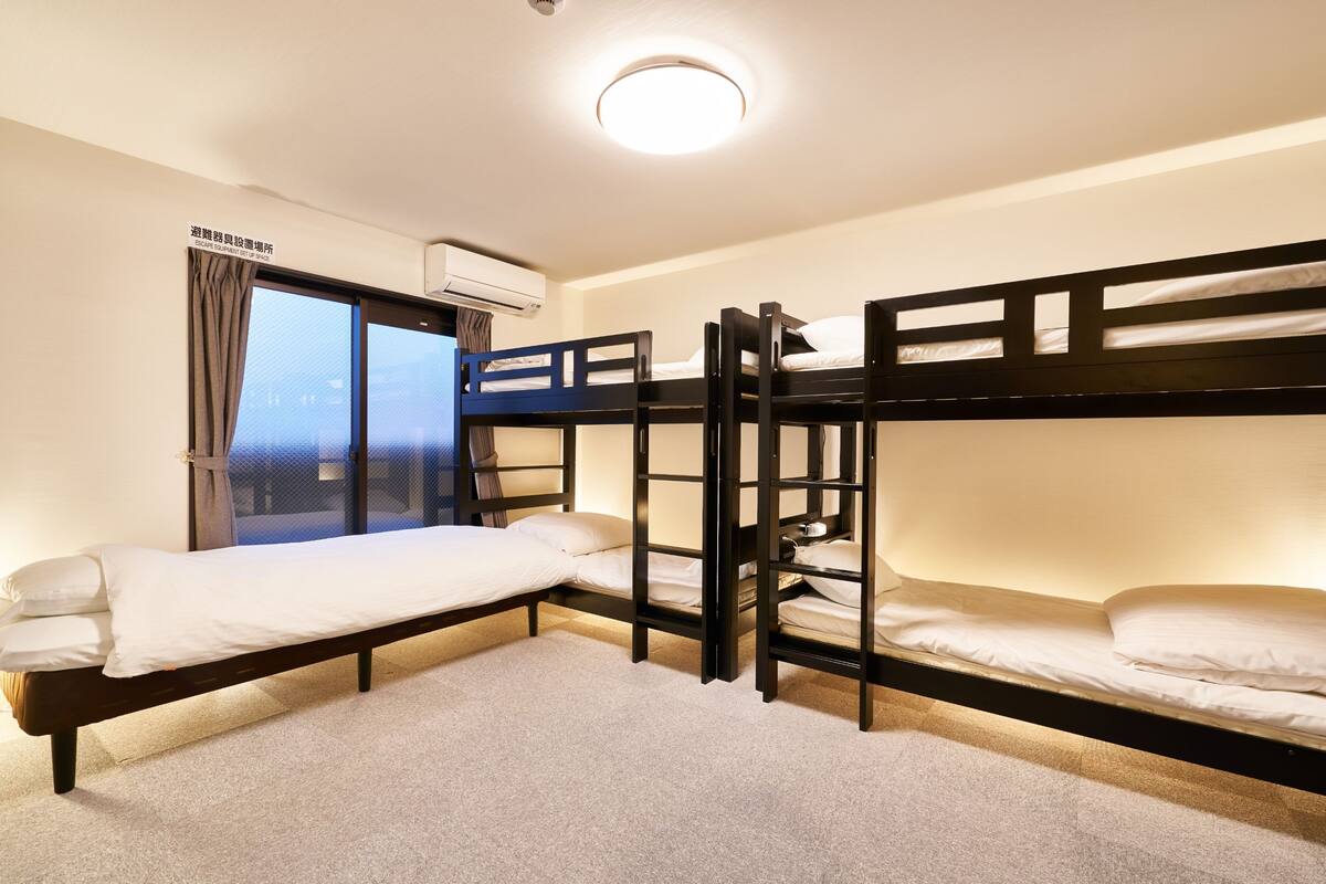 A room with bunk beds, a window with curtains, an air conditioning unit, and a carpeted floor.