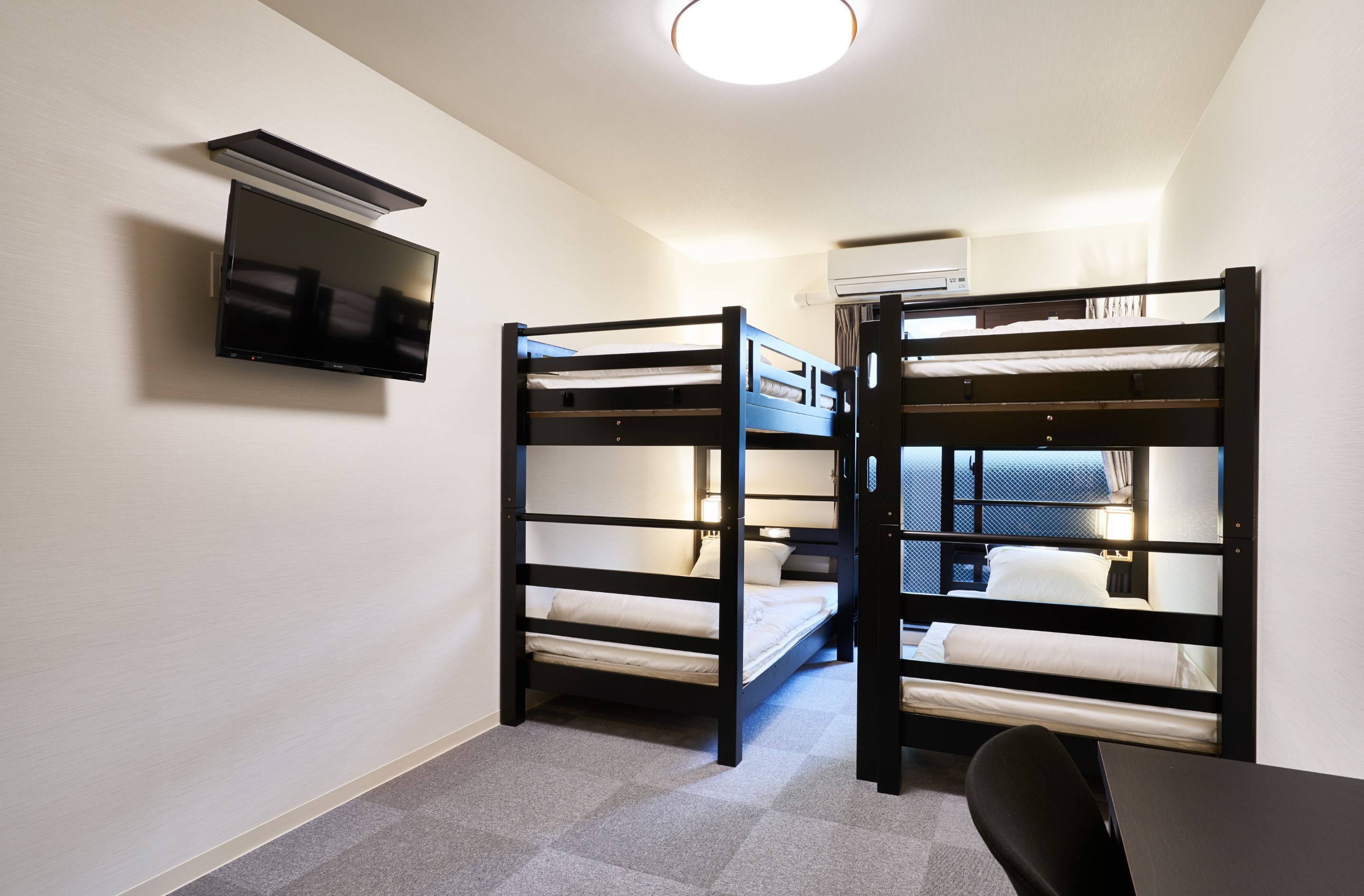 A room with bunk beds, a flat-screen TV mounted on the wall, and an air conditioning unit.