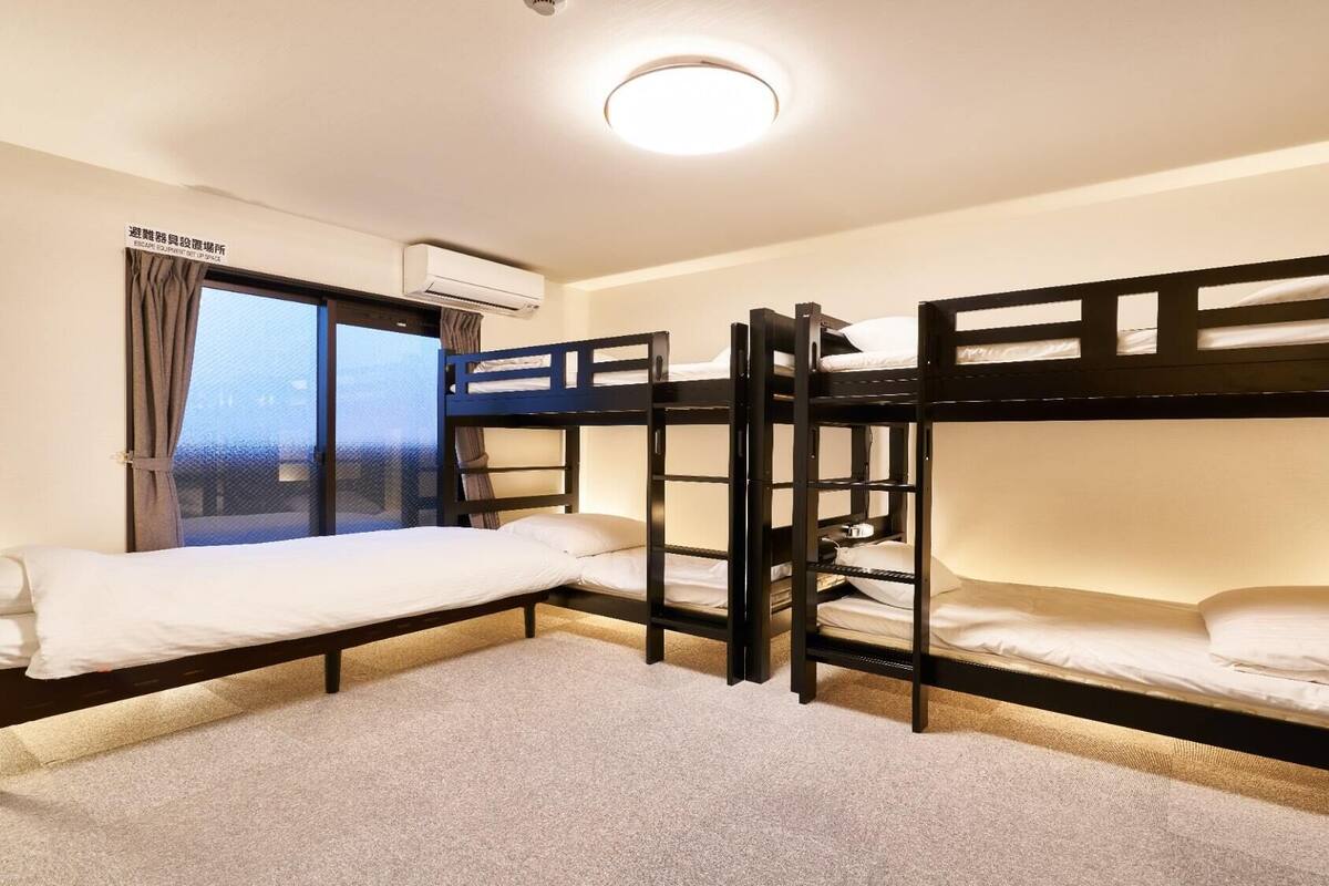 A bunk room with three bunk beds, a window with curtains, an air conditioning unit, and a carpeted floor.