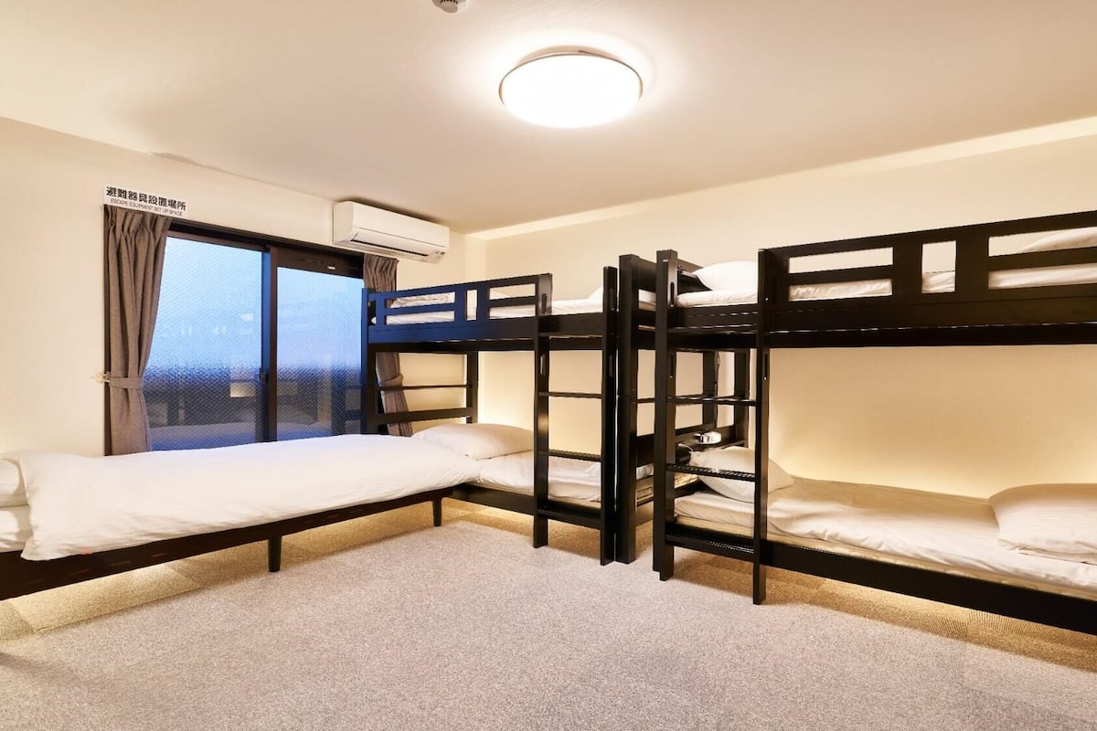A bunk room with three bunk beds, a window with curtains, an air conditioning unit, and a carpeted floor.