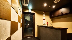 Un couloir avec un comptoir d’accueil, une porte donnant sur une pièce et un climatiseur fixé au mur.