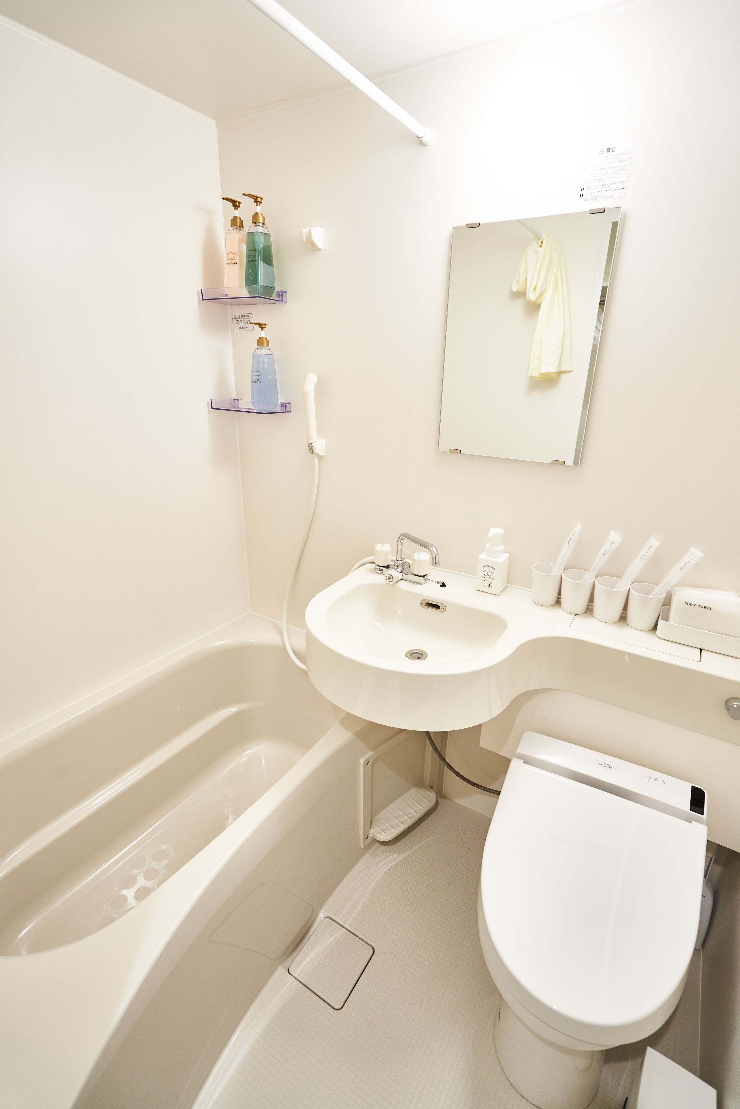 Un baño moderno con bañera, lavamanos e inodoro. Hay estantes con artículos de aseo y un espejo sobre el lavamanos.