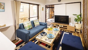 Una sala de estar acogedora con un sofá, una mesa de comedor para dos personas, un televisor y una puerta corrediza que da a otra habitación.