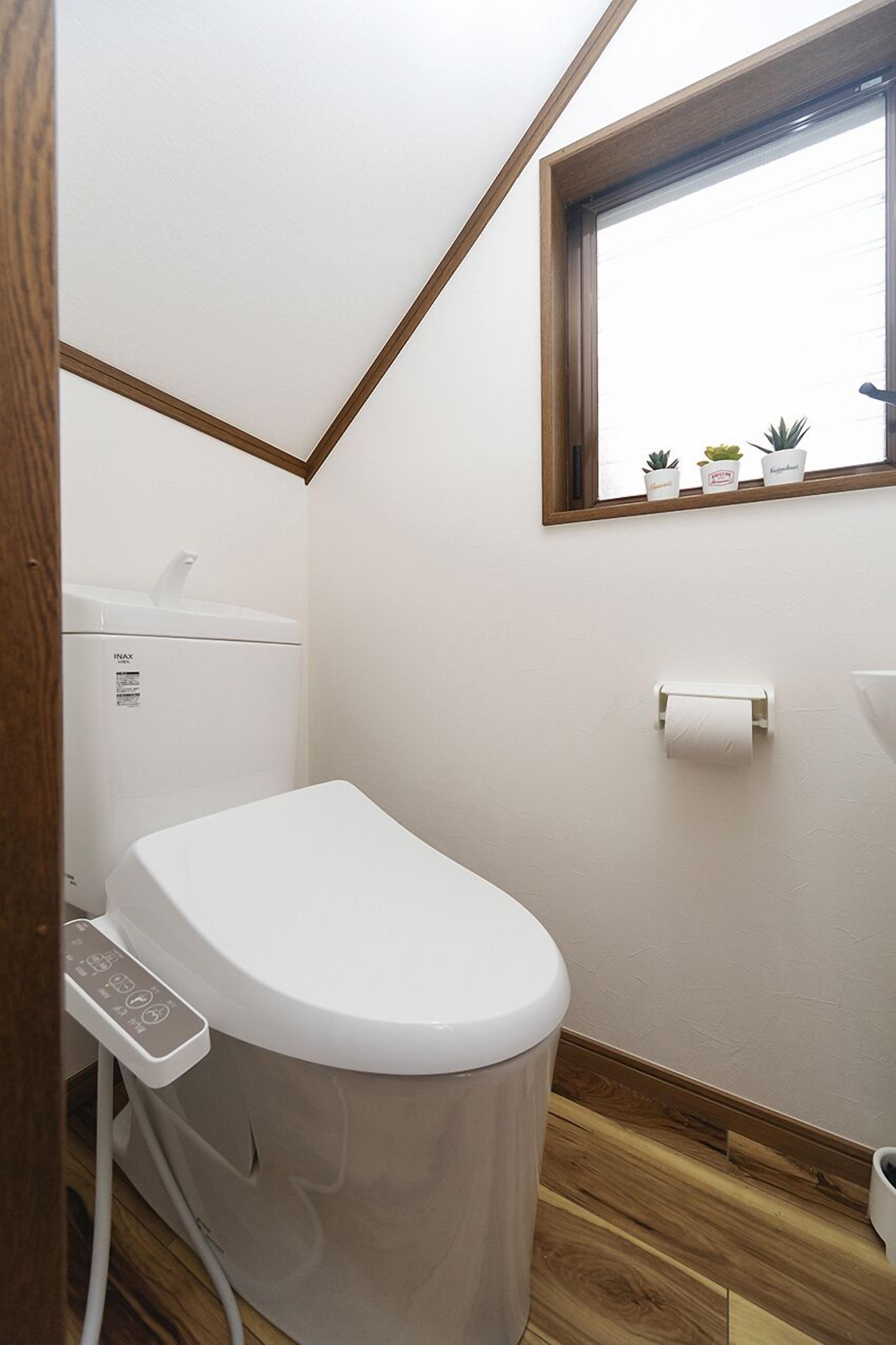 Une petite salle de bain comprenant des toilettes, un lave-linge et une petite fenêtre agrémentée de plantes en pot.