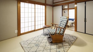 Una habitación japonesa tradicional con suelo de tatami, una silla de madera baja, una mesita redonda y puertas correderas.