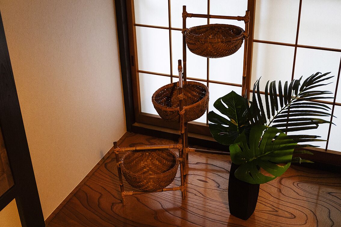 A room with a wooden floor, a bamboo shelf with baskets, and a potted plant.