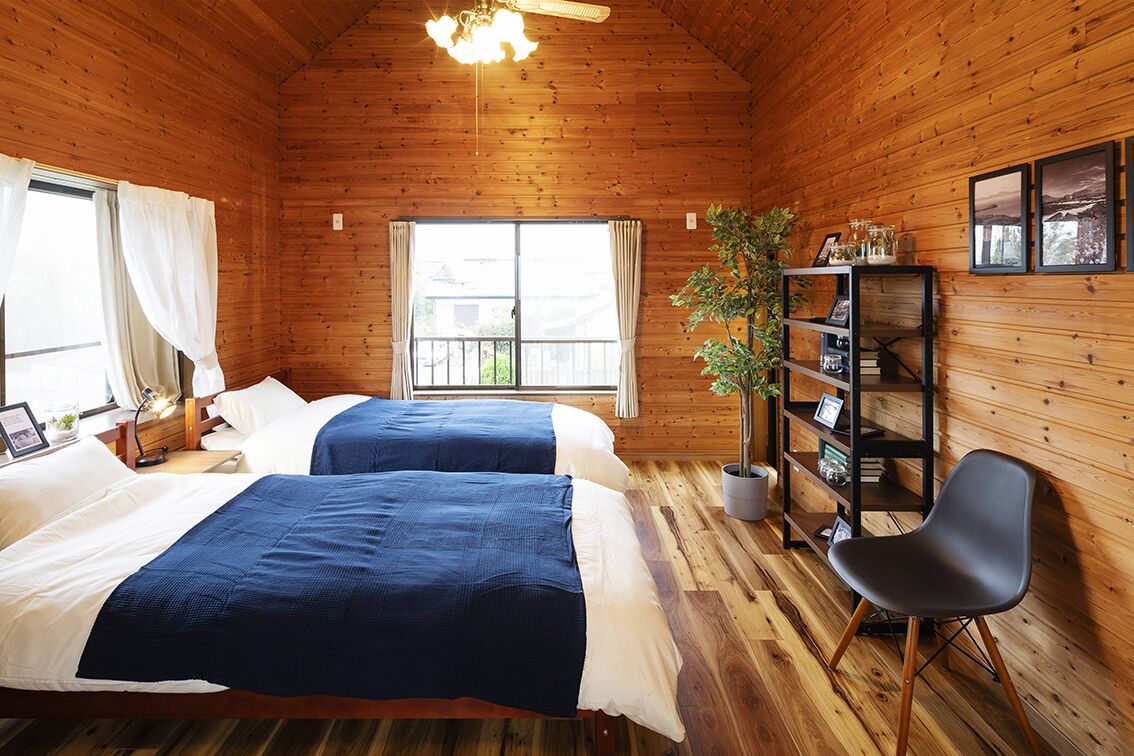 Ein Zimmer in einer Holzhütte mit zwei Betten, einem Bücherregal, einem Sessel und einem Fenster.