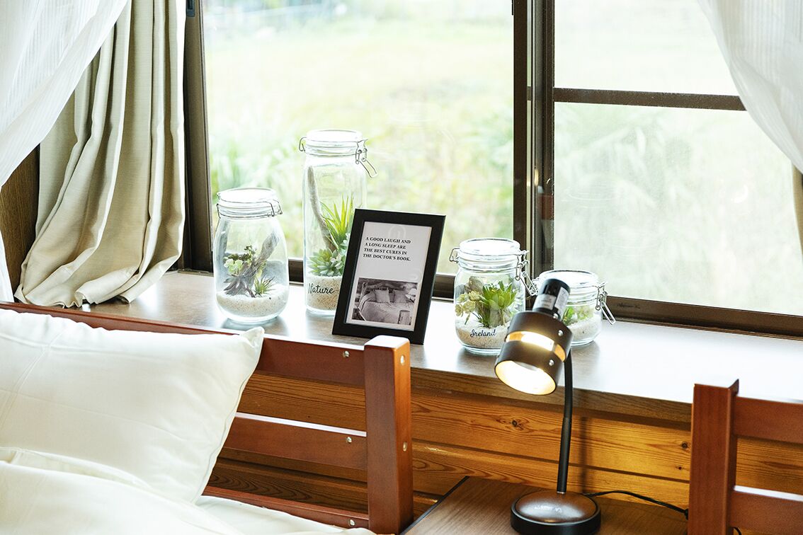 A cozy room with a wooden bed, a desk with a lamp, and a window with curtains.