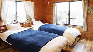 Habitación de cabaña de madera con dos camas, un ventilador de techo y ventanas grandes con cortinas.