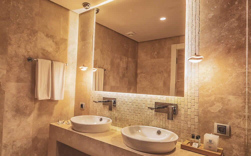 A modern bathroom with two sinks, a large mirror, and a textured wall.