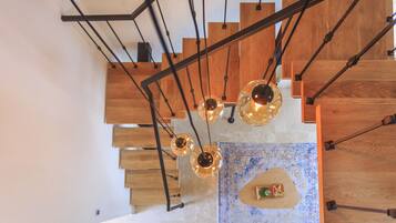 A modern staircase with wooden steps and black metal railings, leading to a landing with a decorative rug and a small table with a glass and a book.