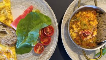 A breakfast setting with a plate of toast, a slice of omelette, fresh tomatoes, and a bowl of soup.