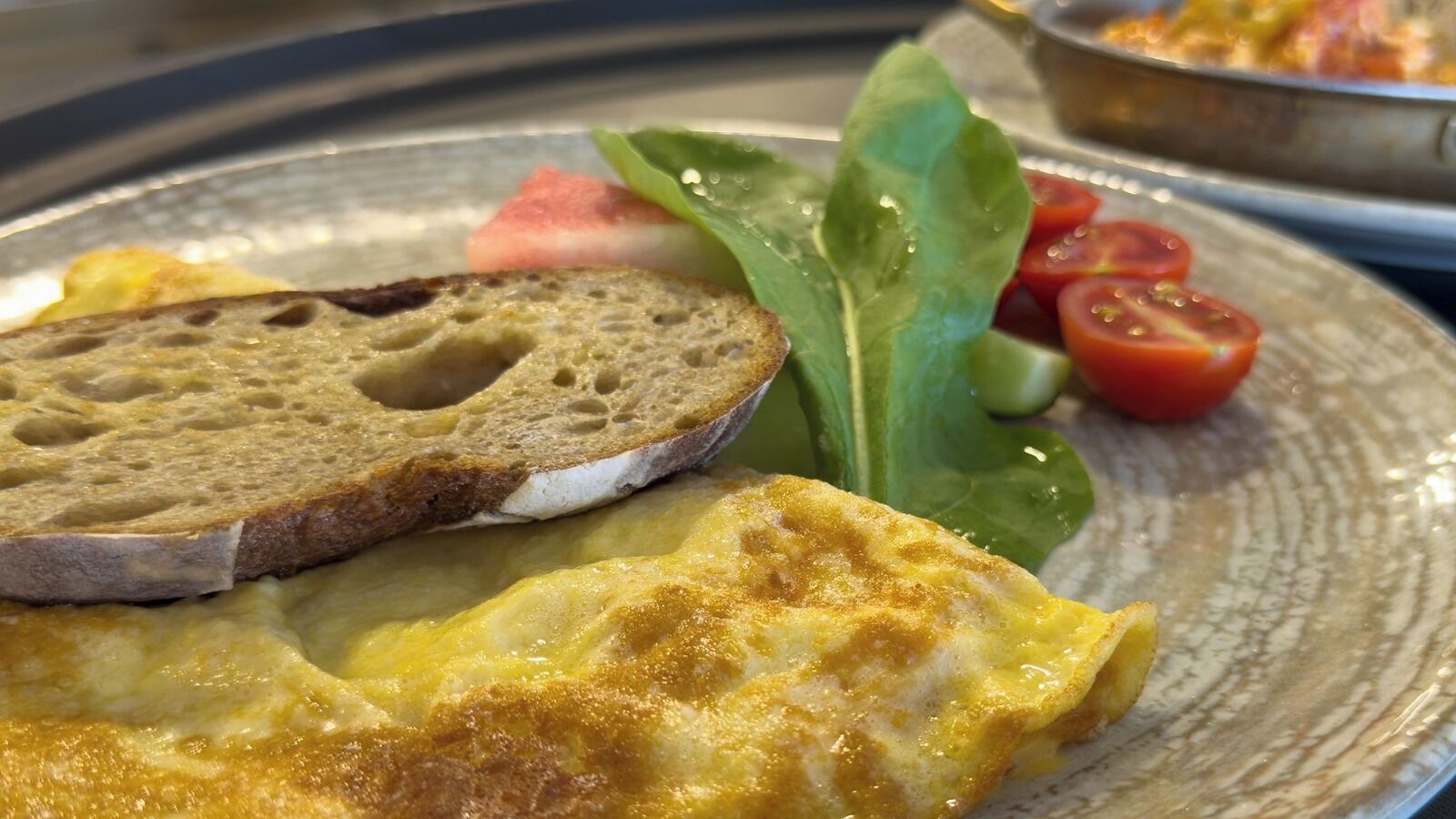 Un plato de desayuno con tortilla, una rebanada de pan y una guarnición de verduras frescas.
