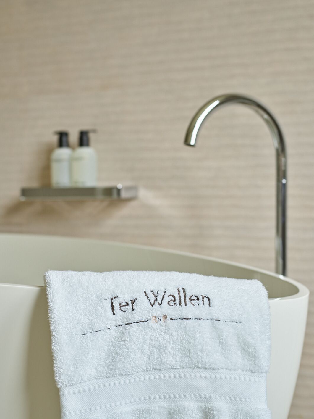 Une salle de bain avec un lavabo blanc, une serviette accrochée au robinet et deux bouteilles posées sur une étagère au-dessus du lavabo.