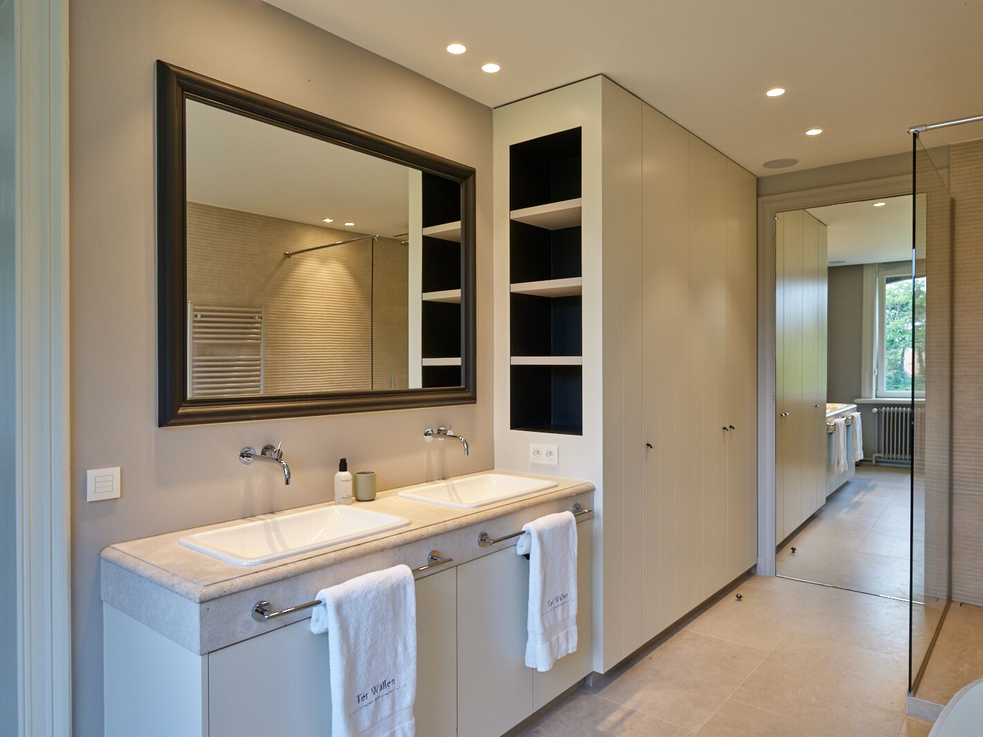 Une salle de bain moderne avec deux lavabos, un grand miroir et des étagères intégrées.