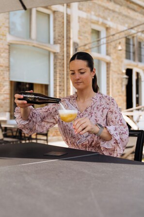 A person pouring a drink into a glass at an outdoor table with a brick building in the background. - Boutique Hotel Ter Wallen (Izegem)