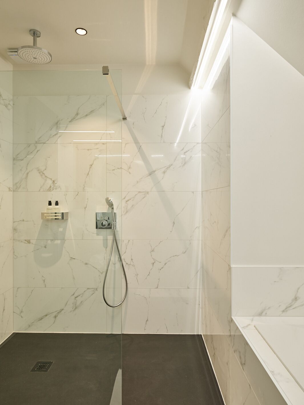 A modern shower with a glass enclosure, marble walls, and a control panel.