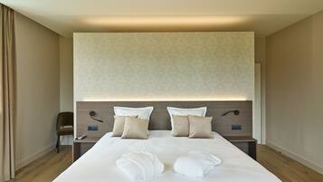 A modern hotel room with a large bed, two bedside tables, a chair, and a headboard with built-in lighting.