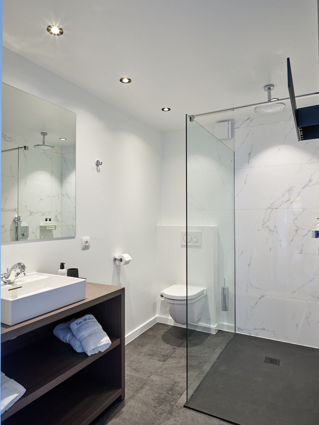 Un baño moderno con ducha acristalada, lavamanos blanco y un espejo grande.