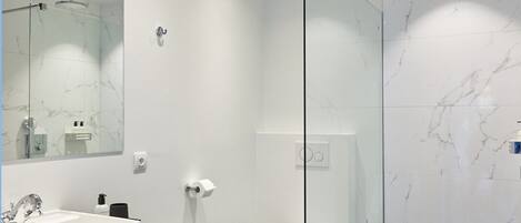 Un baño moderno con ducha acristalada, lavamanos blanco y un espejo grande.