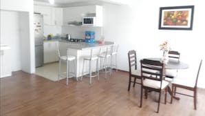 Uma cozinha moderna com armários brancos, uma ilha central com banquetas e uma área de refeições com cadeiras de madeira.