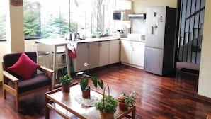 Um espaço de estar compacto com cozinha americana, área de refeições com mesa e cadeiras, e uma janela grande com vista para vegetação.
