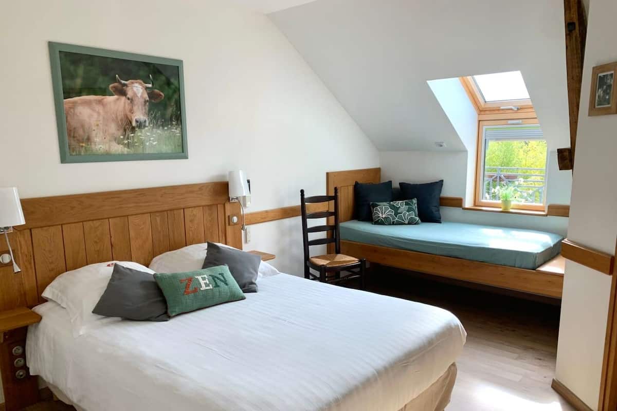 A bedroom with a large bed, a wooden headboard, a window seat, and a painting of a cow.