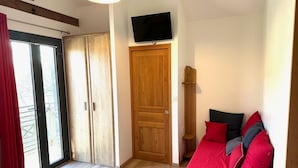 A room with a wooden wardrobe, a television mounted above a door, and a red sofa with pillows. - 50 Route du Gourdon (Cénac-et-Saint-Julien)