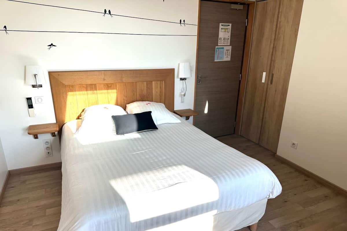 A neatly made bed with a wooden headboard, two bedside lamps, and a small wooden shelf.