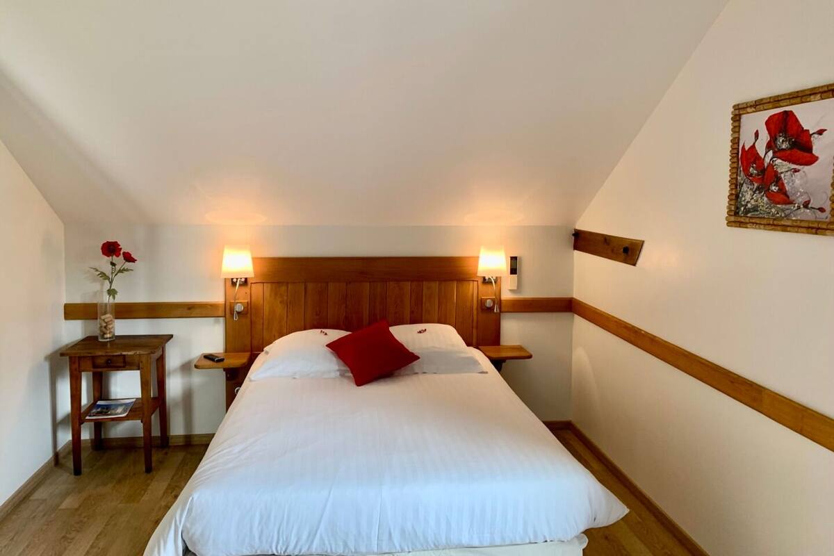 A bedroom with a wooden headboard, two bedside lamps, a wooden nightstand with a vase of flowers, and a framed picture on the wall.