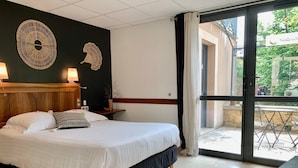 A hotel room with a bed, a wooden headboard, a wall decor, a nightstand, and a view of the outdoor area. - 50 Route du Gourdon (Cénac-et-Saint-Julien)