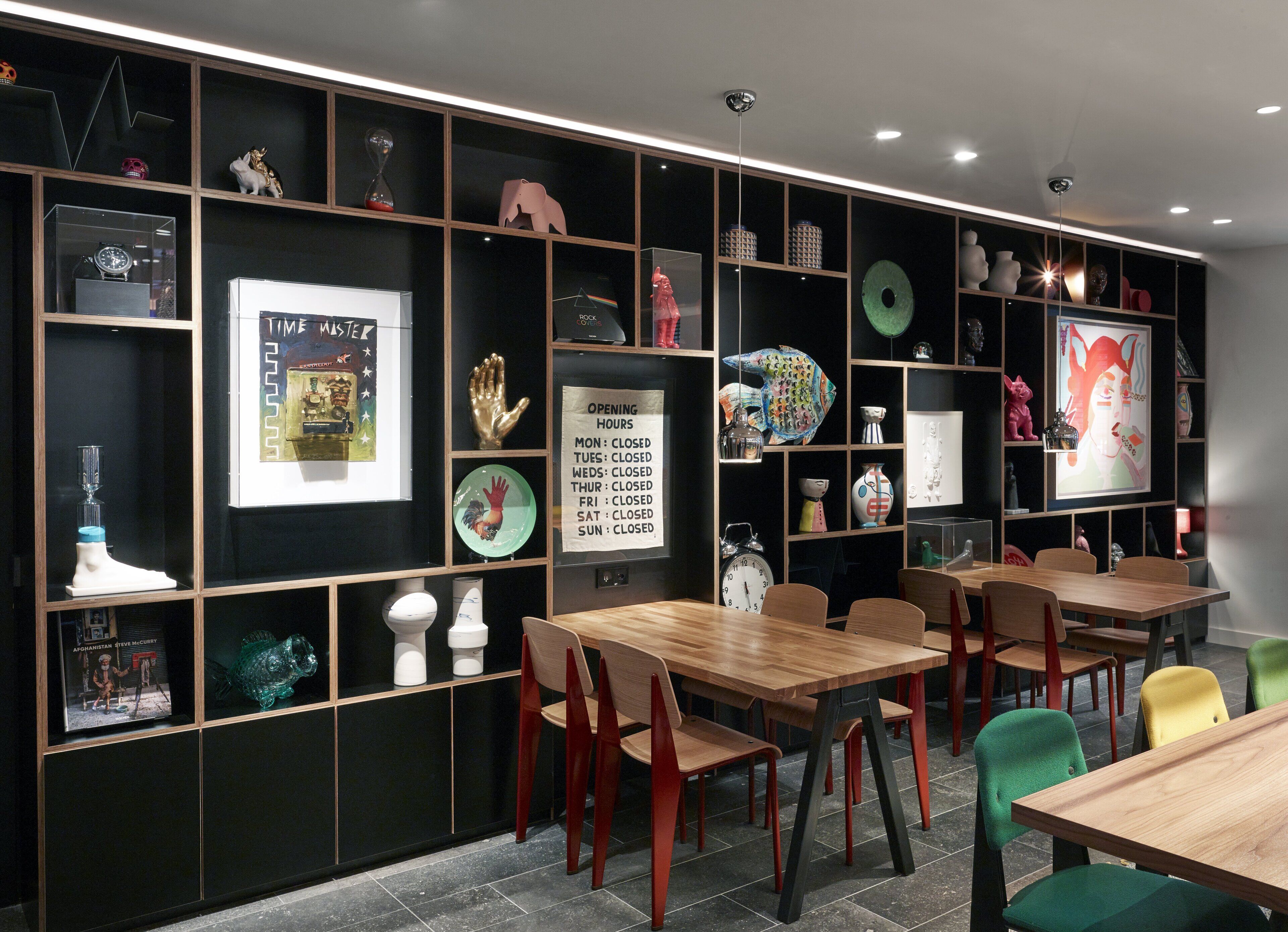 A modern interior with wooden tables and chairs, decorative items on shelves, and a wall clock.