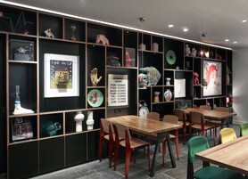 Un interior moderno con mesas y sillas de madera, objetos decorativos en estantes y un reloj de pared.